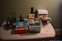 Wide view of the entire lot showing the Wheaton Moon Landing bottle, box of Desert Storm cards, medieval figurines, container with army figures, and Yuengling mug in its box.