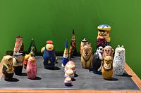 Wide angle photo of 18 varied nesting dolls arranged in rows on a flat surface with green background.