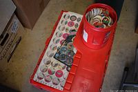 Overview of a red plastic container filled with a large number of pogs and a clear plastic pog display case with pogs inside.