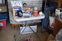 Wide view of table showing various sports memorabilia including mugs, a bobblehead, baseball, and glasses