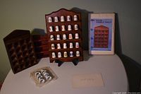 Four wooden shelves for displaying thimbles and small collectibles. One shelf holds vintage company logo thimbles placed in ring-shaped holes on shelves. One shelf remains new in its original unopened box. Additional shelves and loose plain white thimbles are also included.