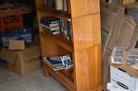 Side view of wooden three-tier bookcase with books, boxes, and some chess pieces visible nearby