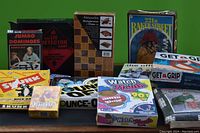 Photo shows various boxed games and cards including Jumbo Dominoes, Antiquarian Backgammon & Chess, Watch Your Mouth, Bounce-Off, Get a Grip, Syink, Canasta Cards, Lie Detector, and 221B Baker Street.