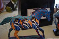 Side view of Cabalito pony figurine featuring painted human figures, blue body with red stars, and orange horse details, showing intricate hand-painted artwork.