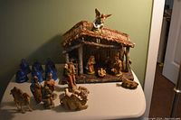 Overview of the nativity stable, various nativity figurines, and six blue porcelain bells on a white table.