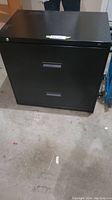 Front view of black 2 drawer HON file cabinet showing rectangular recessed handles, matte black finish and lock on top drawer.