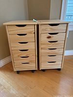 Two natural wood 6-drawer storage cabinets on black rolling casters side by side on hardwood floor against wall corner.