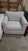 Front view of the pinstriped club chair showing the broad armrests, cushioned seat and back, and fabric upholstery with vertical stripes.