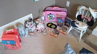 Overview of lot items arranged on carpet, showing Minnie Mouse suitcase, plush kitties, Littlest Pet Shop carrying case, toy records, boxed collectibles, hats, and child's chair