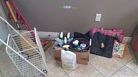 Photo showing a white metal wire shopping cart, cardboard box with cleaning sprays and liquids, reusable bags of different colors lined up against the wall.
