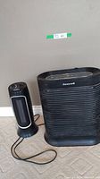 Photo of both Noma electric heater and Honeywell air purifier side by side on carpeted floor against wall.