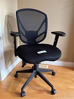 Front view of black ergonomic desk chair showing cushioned seat, mesh back, armrests and caster wheels.