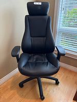 Front view of black leatherette ergonomic desk chair showing padded headrest, contoured back, cushioned seat and five-star caster base