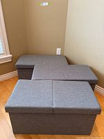 Three light grey storage benches stacked or arranged near a wall, showing solid rectangular shape and padded top seating.