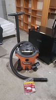 Front view of Ridgid wet/dry vacuum with hose extended and several attachments next to it on the floor.
