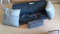 King size denim duvet cover laid out with three denim toss cushions on carpeted floor. Two square cushions show jean pocket designs and one small cylindrical bolster cushion.