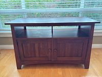 Front view of the dark wooden media/TV stand showing the large open shelf and closed cabinet doors with vertical panel design and round knobs.