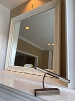 Full view of the shabby chic wooden framed mirror with distressed white paint and beveled glass edges, shown hanging on the wall with the picture light placed below it.
