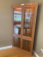 Oak corner hutch featuring glass doors, top section illuminated with interior light, standing in corner of room