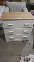 Front view of white 3 drawer dresser with natural pine wood top and white handles.