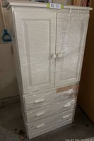 Front view of white pine children's wardrobe wrapped in plastic, showing two cabinet doors and three drawers with some finish damage on lower right side.