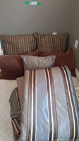 Five cushions, two plaid, two solid brown, one rectangular light beige with brown piping
