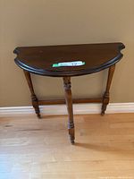 Front view of the half-moon shaped vintage wooden end table showing turned legs and wood finish.