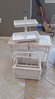 Photo showing the two white wicker side tables stacked, the white two-tier tray on top, and the white wicker magazine rack in front, all arranged on a tiled floor.