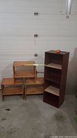Photo showing three low wooden shelves alongside a taller reddish-brown shelving unit in a garage or storage space.