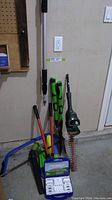 Photo of hedge trimmer, extender bar, cordless rechargeable battery pack in hard case, and several garden tools including pruning loppers with red handles.