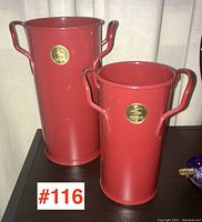 Full view of both red Haws toleware vases showing size difference and gold logo plaques on front