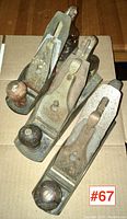 Three vintage woodworking hand planes placed on cardboard, showing metal bodies with wooden handles and knobs.