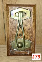 Front view of the antique brass door knocker on oak backing showing the brass knocker and wood grain.
