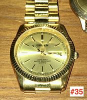 Front view of gold-tone Gruen wrist watch showing dial, hands, Gruen logo, and day-date display at 3 o'clock.