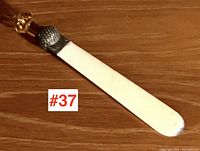 Full length view of the bookmark showing its white celluloid blade with slight tip wear and silver plate thistle cap with glass finial.
