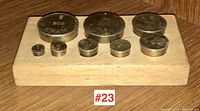 Top view of nine brass scale weights arranged on a wooden holder, each weight showing gram markings