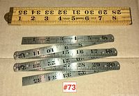 Metal folding rulers unfolded and aligned horizontally with visible measurement markings and slight signs of use.