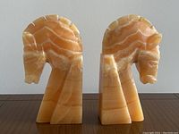 Pair of orange and cream striped onyx alabaster horse head book ends side by side showing the front and left side profiles.