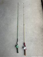Full view of two antique fishing rods side by side against grey surface.