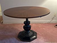 Full view of the round antique table from front with wooden top and black intricate pedestal base, showing height set at mid to low position.