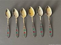 Set of six antique Soviet Russian silver and enamel tea spoons arranged horizontally showing spoon bowls and decorative handles with red and green enamel floral designs.