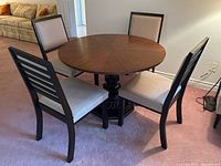 Four dining chairs around a round wooden table (table not included in lot). Two chairs with fully upholstered backs and two with ladder-style backs. Chairs have dark wood frames and light beige upholstery.