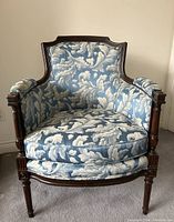 Front view of a vintage armchair showing blue and white floral upholstered fabric with wooden arms and legs.