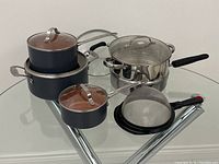Photo showing Gotham Steel cookware set including various sized pots and pans with glass lids, a metal strainer, and a KitchenAid steamer pot.