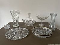 Front view of seven clear crystal and glass items on brown surface including vases, bowls, and trays