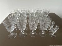 Lot of 18 crystal wine glasses displayed together on a table, showing variety of shapes and patterns.