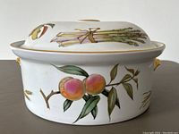 Side view of the white ceramic roasting pan showing hand-painted peaches and leaves with deep gold edging on rim and handles.