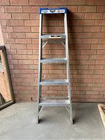 Front view of the aluminum step ladder standing indoors against brick wall.