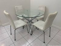 Four white dining chairs arranged in a square around a glass top table to show use and style