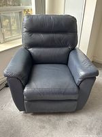 Front view of navy leather electric reclining chair in upright position on carpet near window enhancing lighting and showing the chair's texture.
